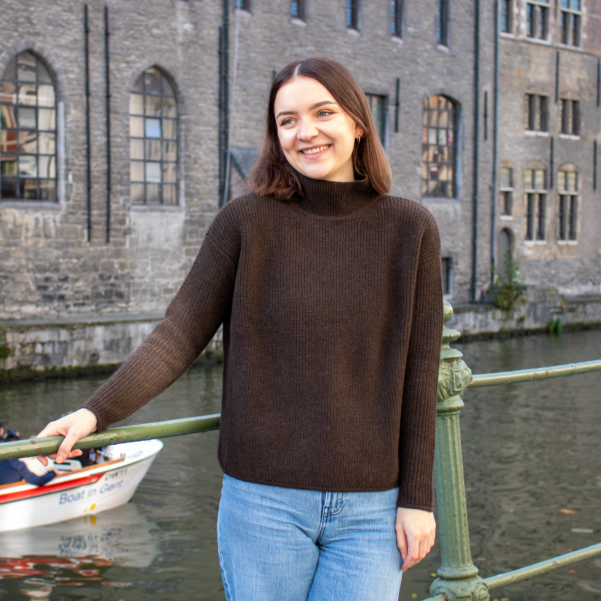 a woman wearing a brown wool sweater and blue jeans on a backgound of old building with channel in the front