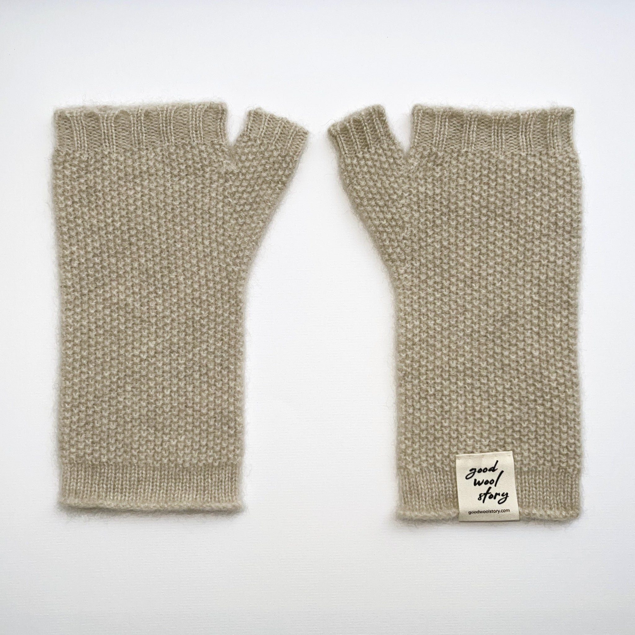 Pair of beige knitted fingerless gloves with a label on a white background