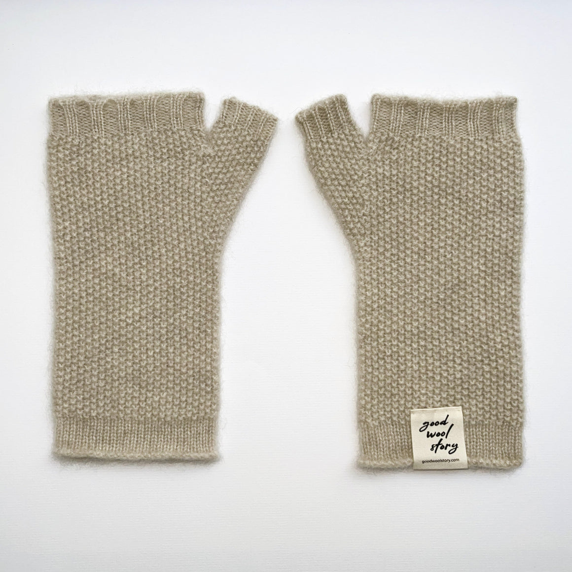 Pair of beige knitted fingerless gloves with a label on a white background