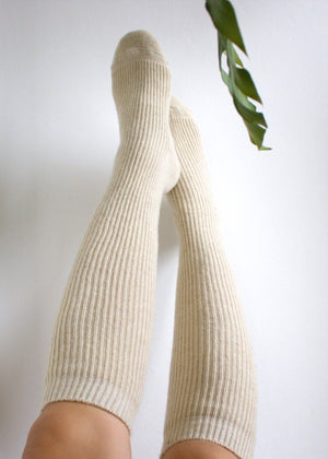 Beige knee-high socks worn by a person on a white background with a green leaf.
