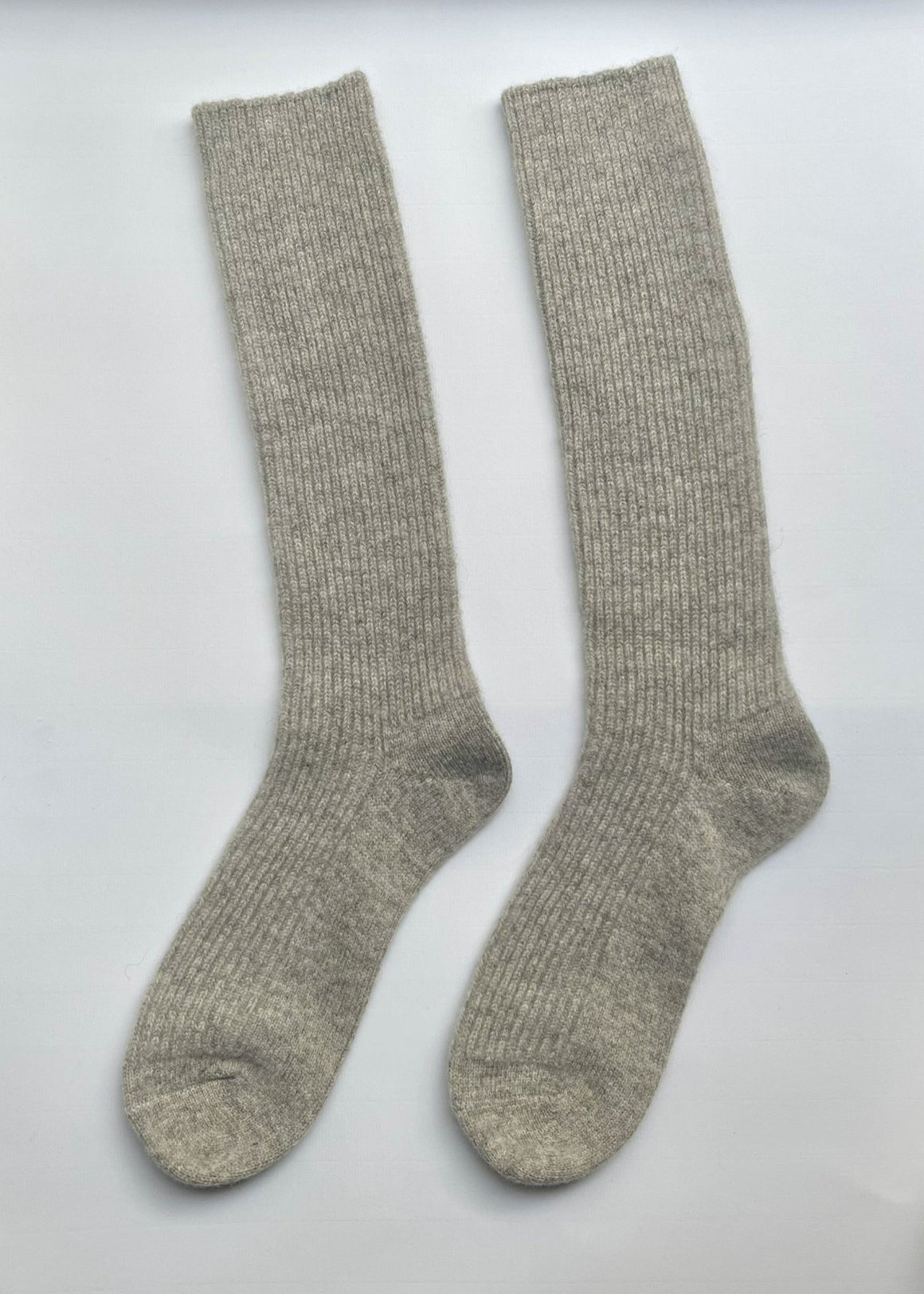 Beige knee-high socks worn by a person on a white background with a green leaf.